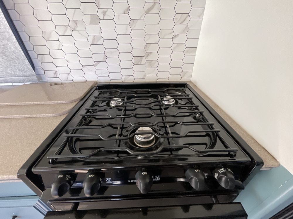 Modern kitchen with 3 burner stove and oven featuring hexagonal tile backsplash