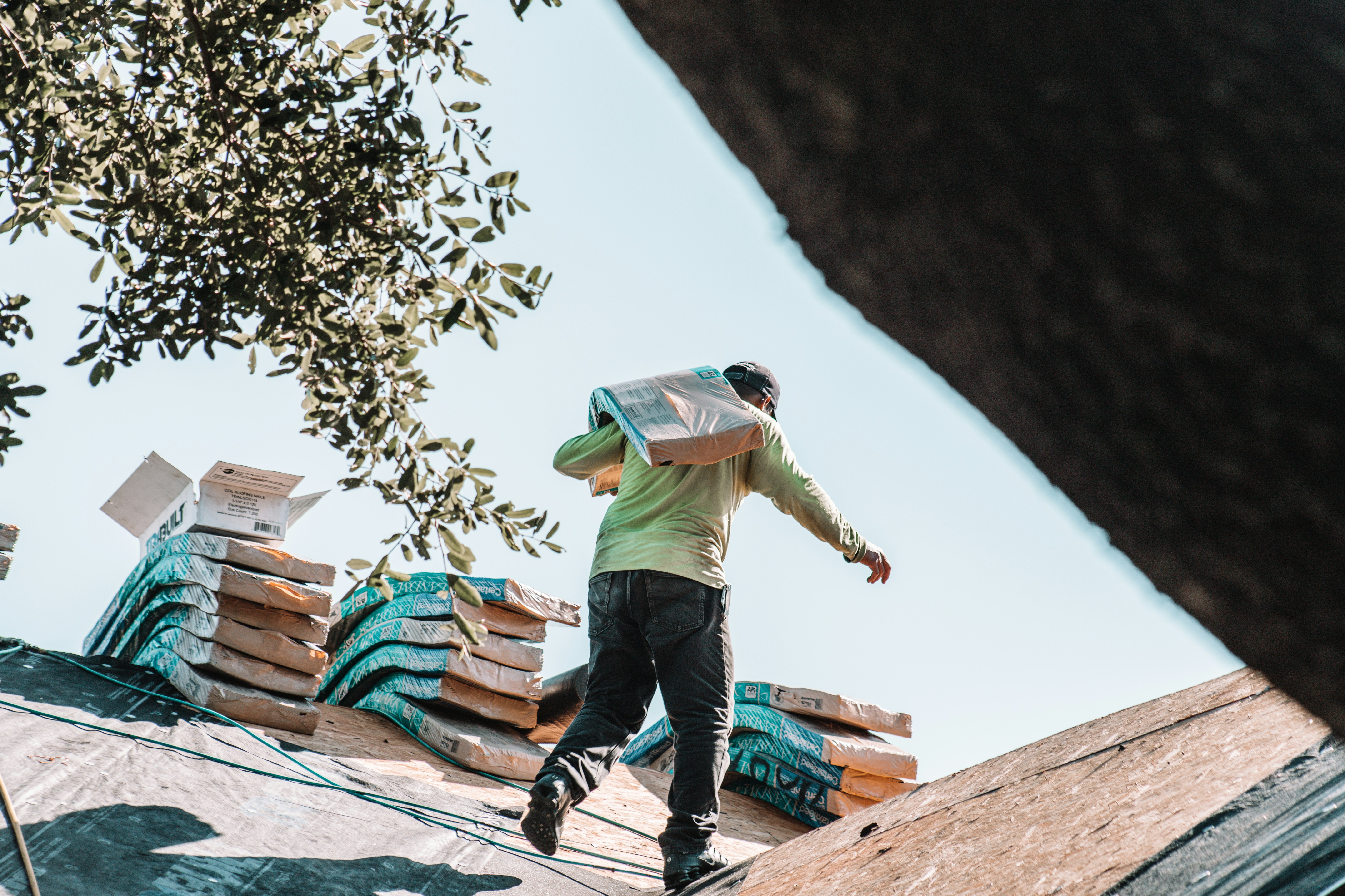 Roofing contractor carrying shingles on roof with stacks of roofing materials in Abilene Texas