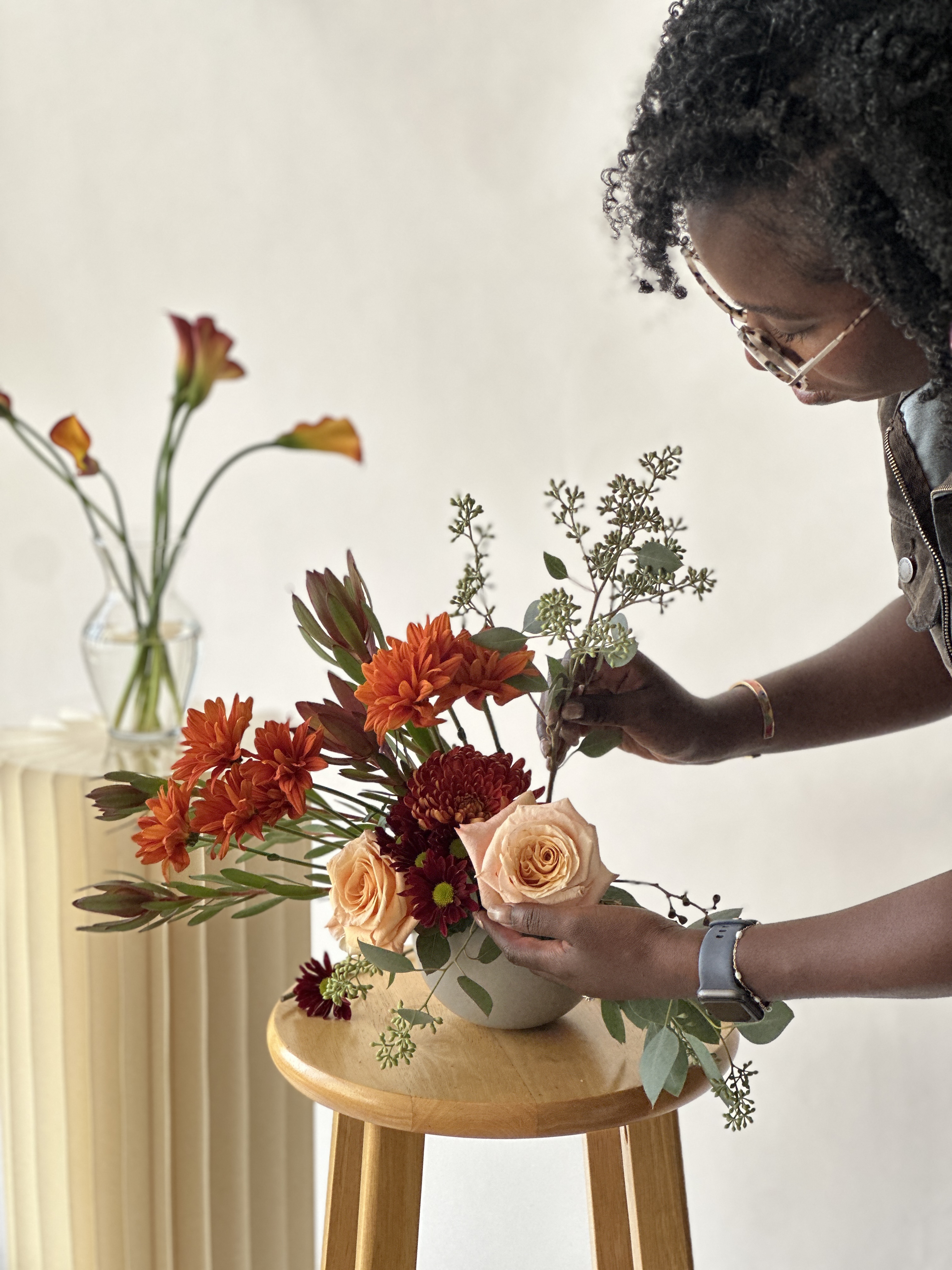 Person creating a floral arrangement with vibrant orange and burgundy flowers