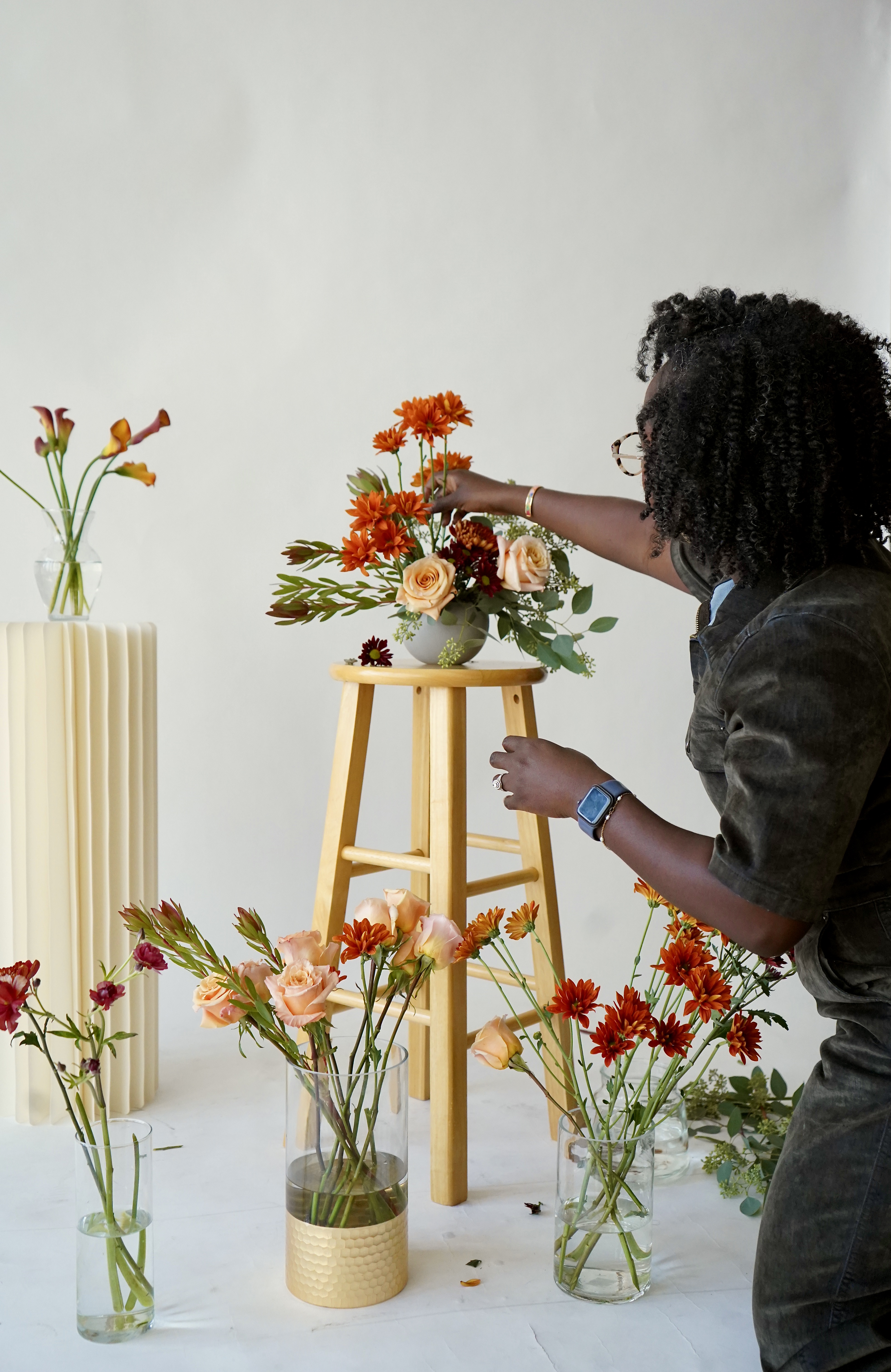 Person actively working on floral arrangements in a workshop setting, with various flowers, vases, and materials around them