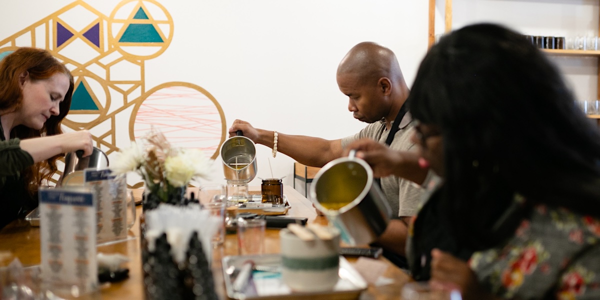 People actively working together in a candle making workshop, pouring wax and creating candles with professional equipment and materials