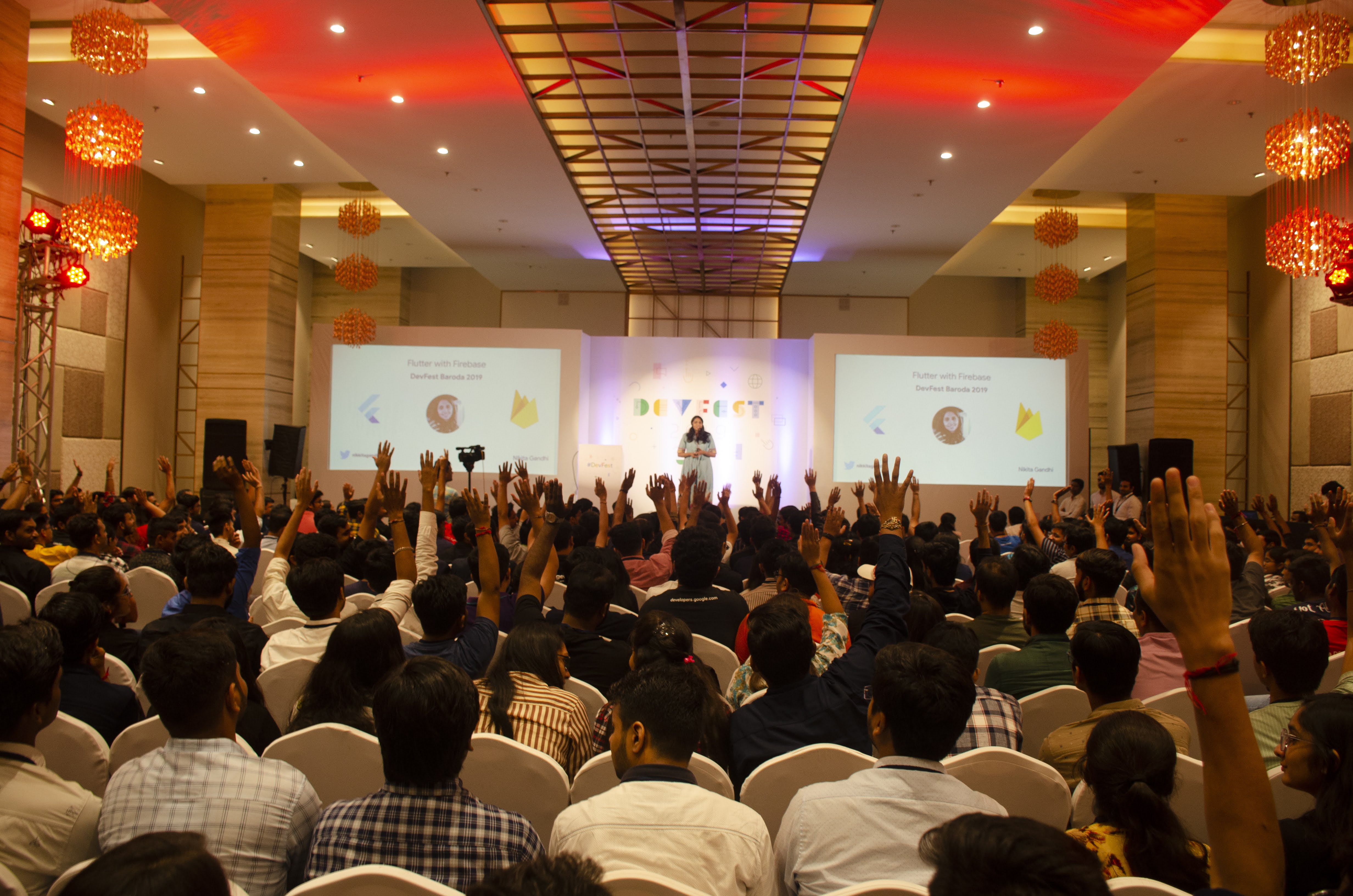 DevFest conference hall packed with hundreds of engaged attendees raising their hands as a speaker presents on stage
